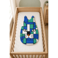 A baby sleep sack or sleeping bag with a colorful geometric cat face design, displayed on a white mattress inside a light wood crib.