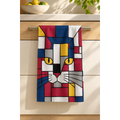 A kitchen towel featuring a geometric cat design in red, blue, yellow, white, and gray, hanging from a metal handle on a wooden kitchen cabinet.