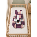A baby sleep bag with a geometric cat face design in purple, pink, white, and black, displayed on a white mattress inside a light wood crib.